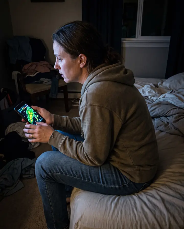 A woman sitting on her bed at night, lit by her phone screen
